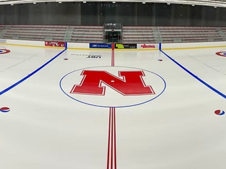 Red "N" logo on a white ice hockey rink with blue and red lines, in a large indoor arena.