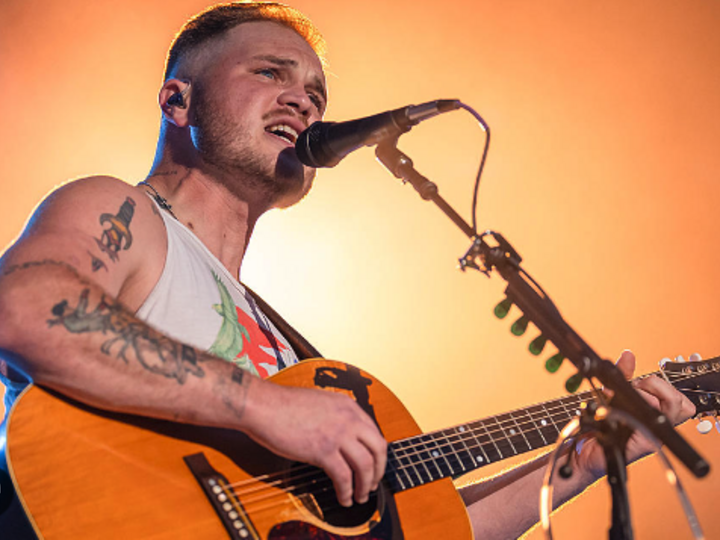 Musician playing acoustic guitar under warm stage lighting.